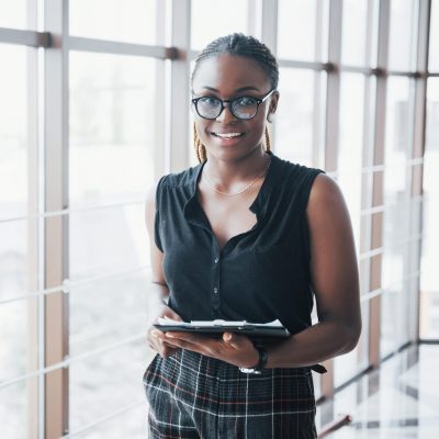A thoughtful African American business woman wearing glasses holding documents.